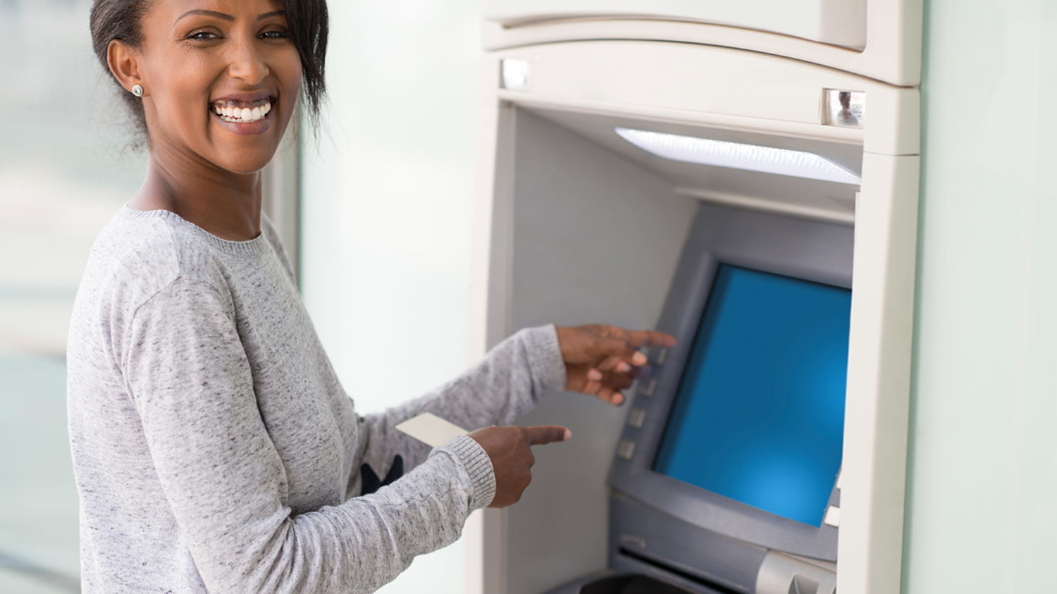 Frau mit Kreditkarte zeigt lachend auf das Display eines Geldautomaten